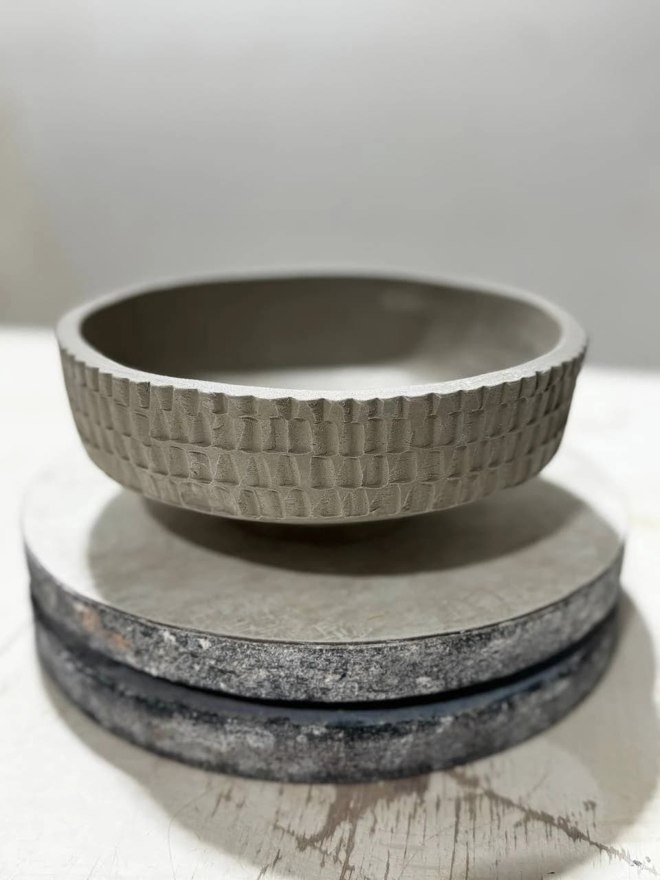 Unglazed clay bowl with a carved repeating exterior texture, resting on a studio banding wheel.